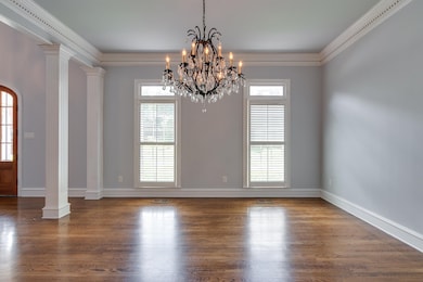 Unfurnished room featuring decorative columns, wood finished floors, a chandelier, ornamental molding, and arched walkways
