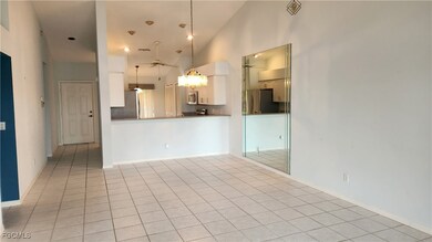 Kitchen with stainless steel appliances, pendant lighting, light tile patterned flooring, white cabinetry, and a towering ceiling
