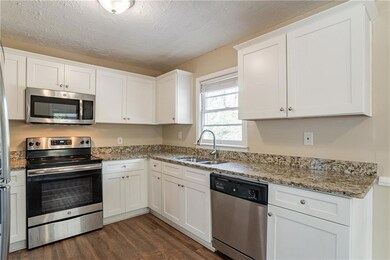 Kitchen with dark hardwood / wood-style floors, sink, white cabinetry, light stone countertops, and stainless steel appliances