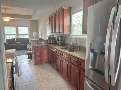 Kitchen featuring stainless steel appliances, light tile patterned floors, a ceiling fan, open floor plan, and stone counters