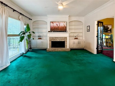 Unfurnished living room featuring dark carpet, ornamental molding, built in shelves, healthy amount of natural light, and a stone fireplace