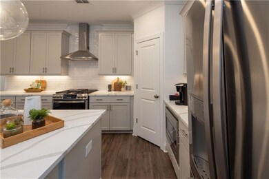 Kitchen with stainless steel appliances, wall chimney exhaust hood, dark wood-style floors, decorative backsplash, and light stone countertops