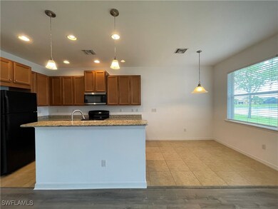 Kitchen featuring freestanding refrigerator, recessed lighting, stainless steel microwave, light stone countertops, and pendant lighting