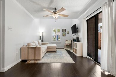 Living room with dark wood-style flooring, a textured ceiling, crown molding, ceiling fan, and a fireplace