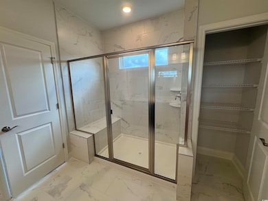 Full bath featuring marble look tiles, a shower stall, and a walk in closet