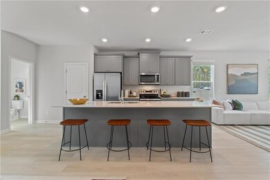 Kitchen with gray cabinetry, stainless steel appliances, a kitchen breakfast bar, a center island with sink, and recessed lighting
