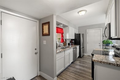 Kitchen with stainless steel appliances, light stone counters, white cabinets, and dark wood-style floors