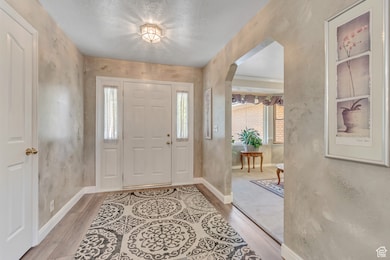 Foyer featuring a textured ceiling, arched walkways, light wood finished floors, and a textured wall