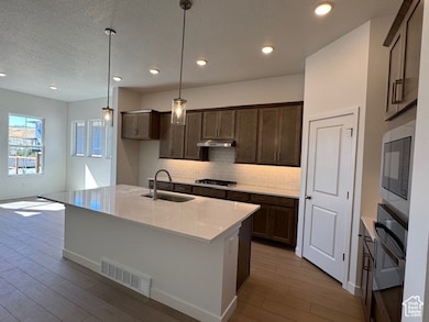 Kitchen featuring decorative light fixtures, tasteful backsplash, light stone counters, an island with sink, and dark brown cabinetry