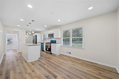 Kitchen with white cabinets, hanging light fixtures, a kitchen island, light hardwood / wood-style floors, and stainless steel appliances