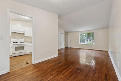 Unfurnished living room with dark wood-style flooring, vaulted ceiling, and a textured ceiling