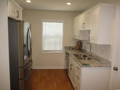 Kitchen with appliances with stainless steel finishes, dark wood-style floors, white cabinetry, light stone countertops, and tasteful backsplash