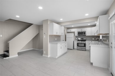 Kitchen with stainless steel appliances, white cabinets, backsplash, recessed lighting, and light stone countertops