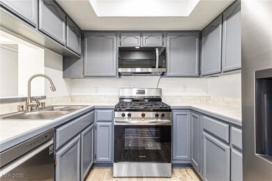 Kitchen featuring gray cabinetry, tile countertops, appliances with stainless steel finishes, and light wood-style floors