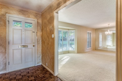 Foyer entrance with a textured ceiling, crown molding, a chandelier, and parquet flooring
