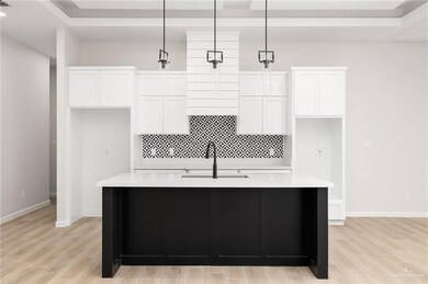 Kitchen with a center island with sink, pendant lighting, light hardwood / wood-style flooring, and white cabinetry
