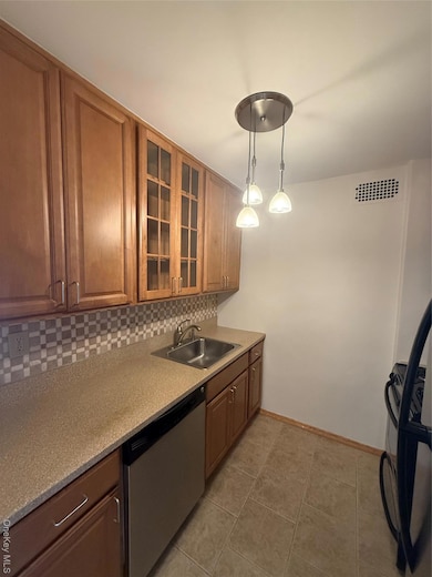 Kitchen with dishwashing machine, glass insert cabinets, decorative backsplash, decorative light fixtures, and brown cabinets