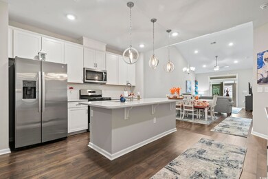 Kitchen featuring stainless steel appliances, dark wood-type flooring, white cabinets, decorative light fixtures, and recessed lighting