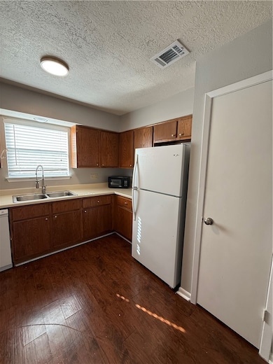 Kitchen featuring light countertops, dark wood-type flooring, refrigerator, a textured ceiling, and brown cabinetry