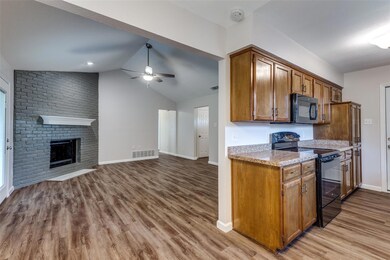 Kitchen featuring black appliances, a brick fireplace, hardwood / wood-style floors, ceiling fan, and vaulted ceiling