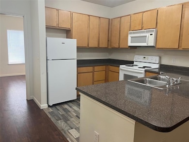 Kitchen featuring white appliances, a peninsula, dark wood-style flooring, and dark countertops