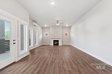 Unfurnished living room featuring a warm lit fireplace, ceiling fan, wood finished floors, a wall mounted AC, and recessed lighting