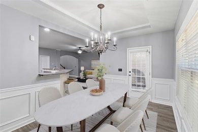 Dining area with a decorative wall, wainscoting, arched walkways, wood finished floors, and a tray ceiling