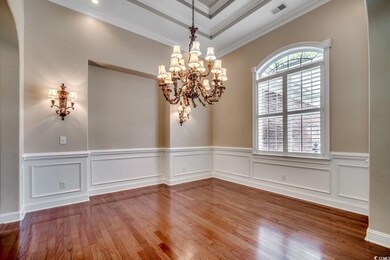 Unfurnished dining area featuring hardwood / wood-style floors, a chandelier, crown molding, a tray ceiling, and a decorative wall