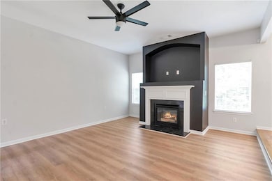 Unfurnished living room featuring healthy amount of natural light, a fireplace with flush hearth, a ceiling fan, and light wood-style floors