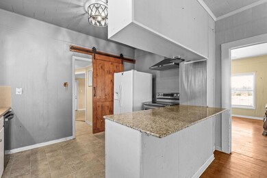 Kitchen featuring stainless steel range with electric cooktop, wood walls, white fridge with ice dispenser, crown molding, and a barn door