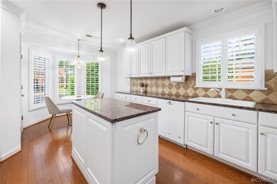 Kitchen featuring hardwood floors, center island with, crown molding, pendant lighting, stone countertops, white cabinets, white dishwasher, hardwood flooring, and granite countertop