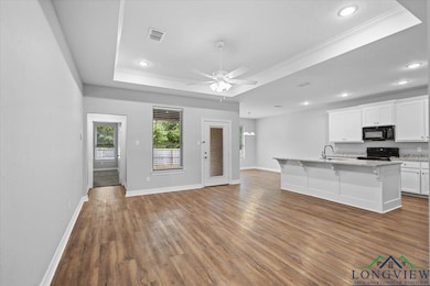 Unfurnished living room with a raised ceiling, dark wood-style flooring, ornamental molding, a ceiling fan, and recessed lighting