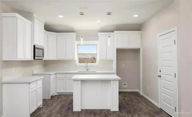 Kitchen featuring stainless steel microwave, a sink, a center island, white cabinets, and dark wood finished floors