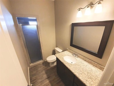 Bathroom with toilet, wood finished floors, vanity, and a stall shower