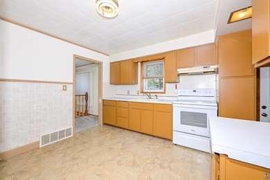 Kitchen featuring electric range, under cabinet range hood, a sink, light countertops, and wainscoting