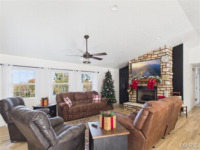 Living area featuring light wood finished floors, lofted ceiling, plenty of natural light, ceiling fan, and a stone fireplace
