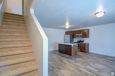 Kitchen featuring appliances with stainless steel finishes, an island with sink, dark wood finished floors, and light stone counters