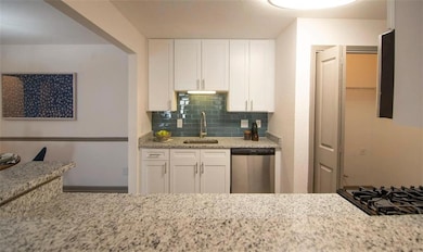 Kitchen featuring dishwasher, light stone countertops, white cabinetry, sink, and tasteful backsplash