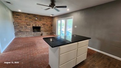Kitchen featuring white cabinetry, brick wall, dark countertops, a fireplace, and dark wood-type flooring
