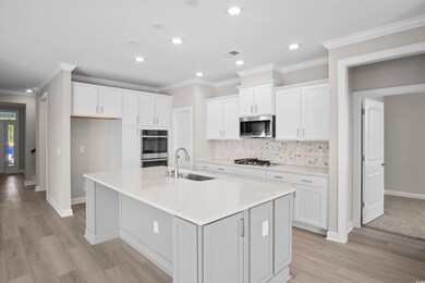 Kitchen featuring white cabinets, crown molding, a center island with sink, decorative backsplash, and light wood-style floors