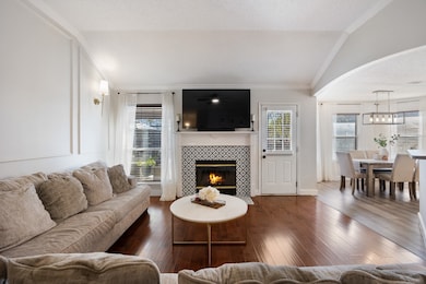 Living area featuring hardwood / wood-style flooring, a tiled fireplace, a textured ceiling, ornamental molding, and lofted ceiling