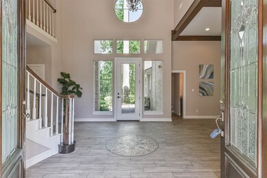 A grand foyer with a soaring two-story ceiling and a beautiful chandelier is bathed in abundant natural sunlight streaming in from transom windows on either side of the foyer. Wood-look tile floors are punctuated by a mosaic tile design in the center.