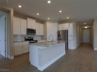 Kitchen featuring appliances with stainless steel finishes, white cabinets, dark wood-style floors, light stone counters, and recessed lighting