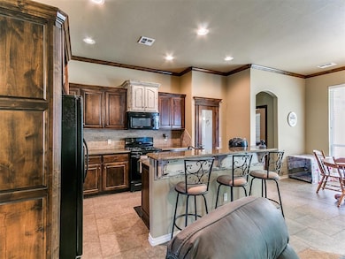 Kitchen with black appliances, arched walkways, a kitchen breakfast bar, decorative backsplash, and ornamental molding