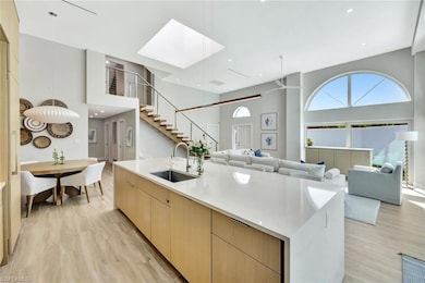 Kitchen featuring light wood finished floors, a high ceiling, light brown cabinetry, a sink, and modern cabinets