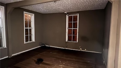 Empty room with a textured ceiling, wood finished floors, and baseboards
