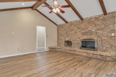 Unfurnished living room with a fireplace, wood finished floors, beam ceiling, and ceiling fan