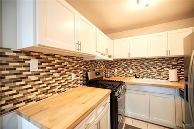 Kitchen featuring stainless steel appliances, wooden counters, sink, white cabinets, and decorative backsplash