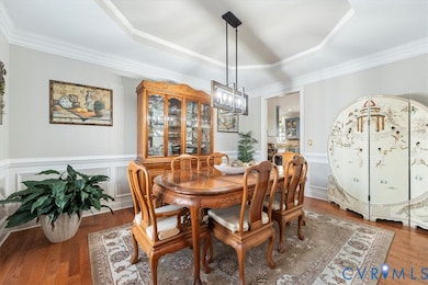Dining area with a raised ceiling, wood finished floors, a wainscoted wall, ornamental molding, and a decorative wall