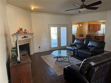 Living room featuring crown molding, a chandelier, dark wood finished floors, a tiled fireplace, and a ceiling fan